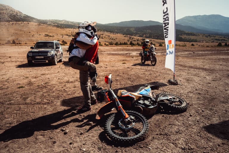 Rider picking up a fallen bike on a dusty track