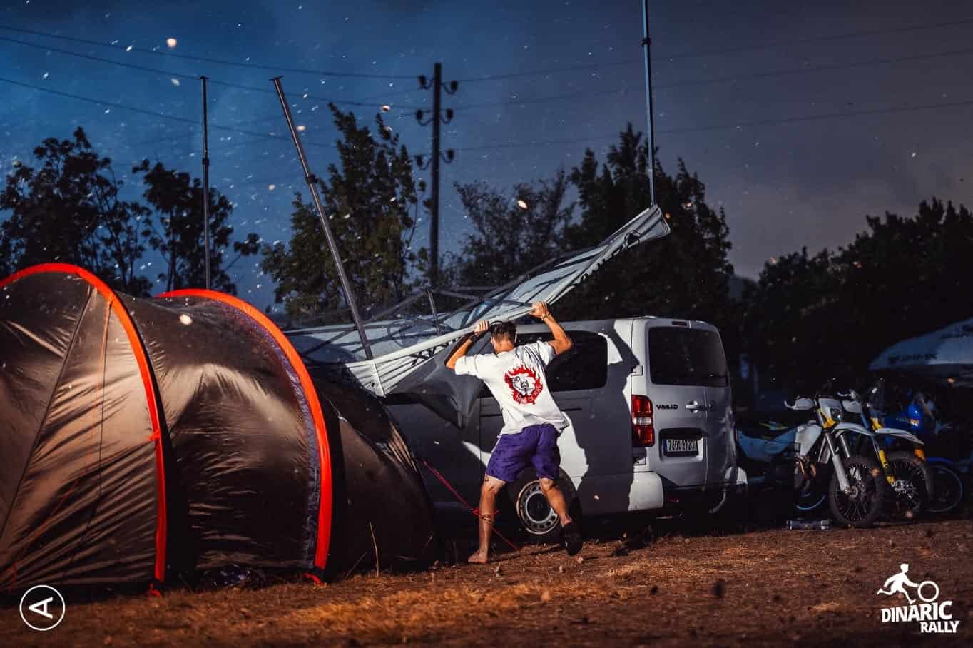 Rider pitching a tent in the Dinaric Rally bivouac at dusk