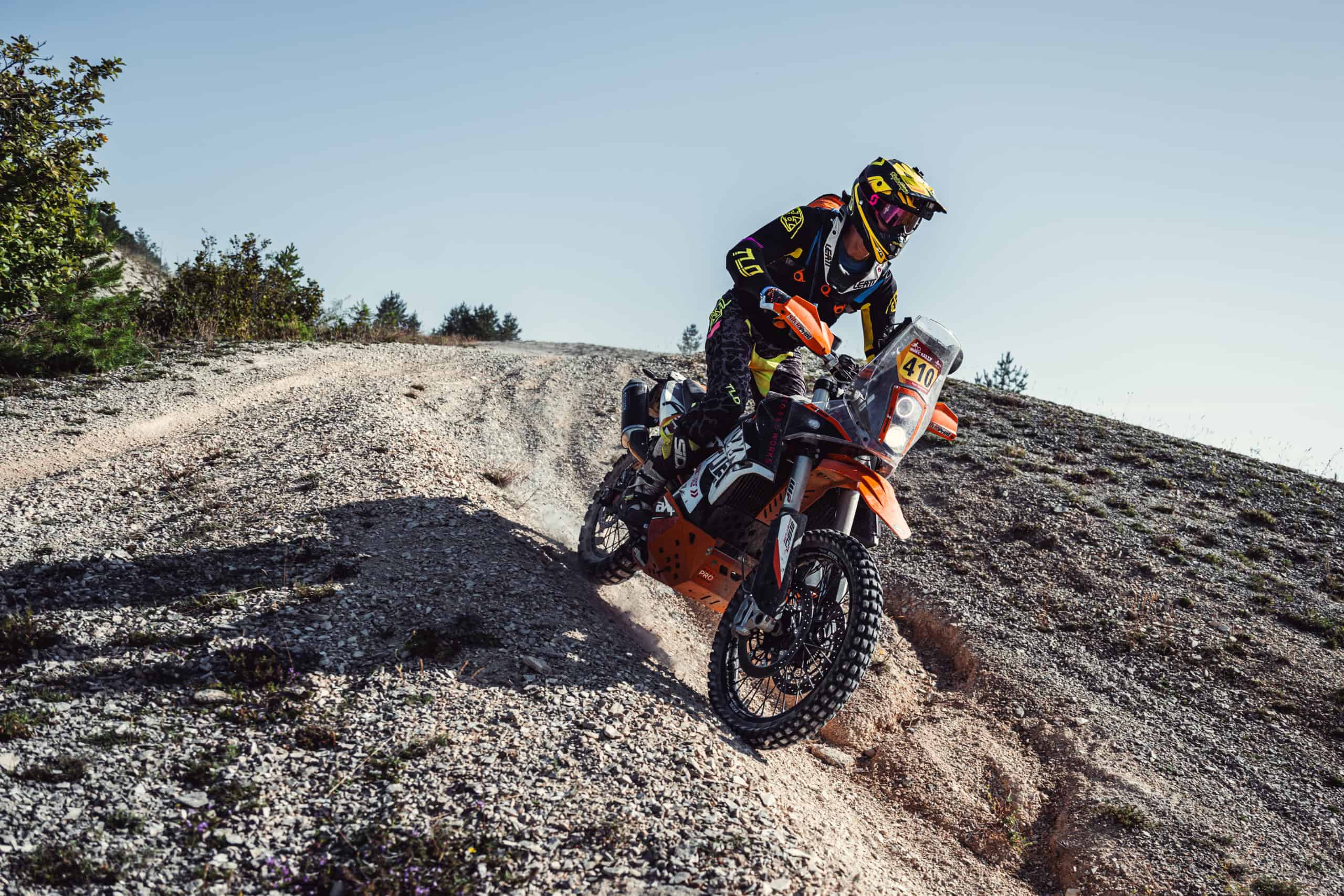 Rally rider on an orange bike climbing a loose gravel slope