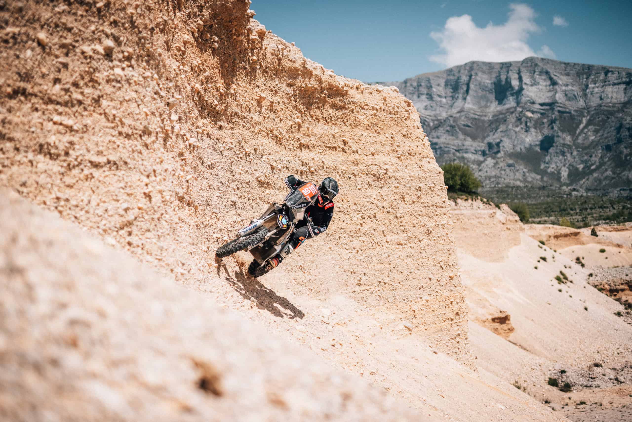 Pilota di rally su un pendio roccioso chiaro sotto le montagne